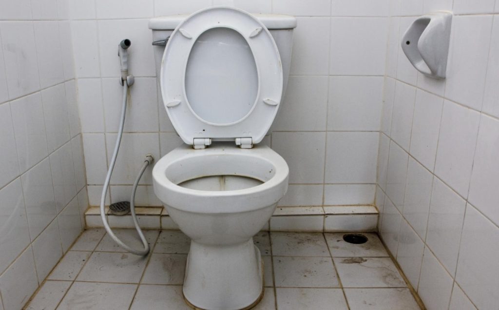 Persona abriendo la puerta de un baño público con la mano, una de las superficies señaladas por los científicos como las más contaminadas del servicio, muy por encima del asiento del inodoro según los estudios más recientes